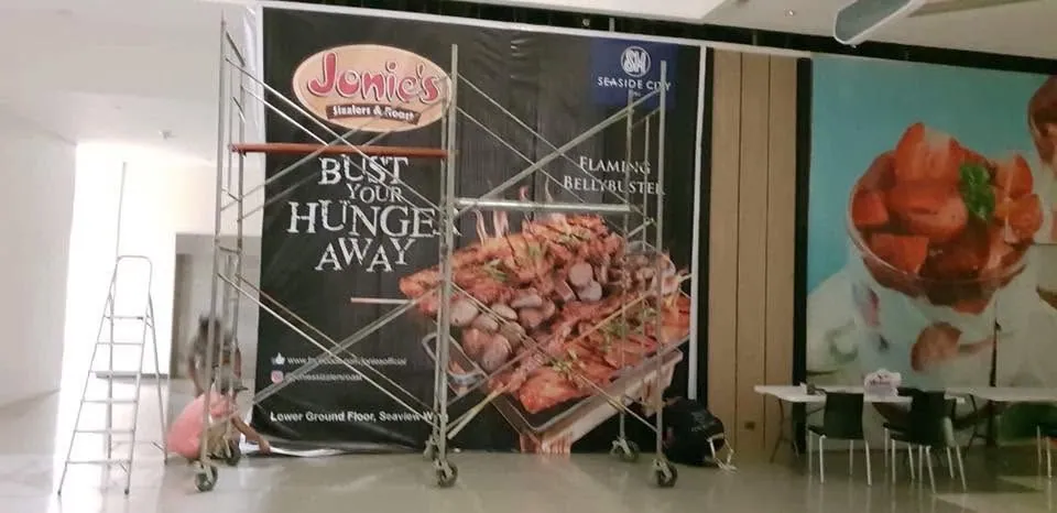 MCAV crew installing a Jonie's Sizzlers + Roast tarpaulin at SM Seaside City, Cebu